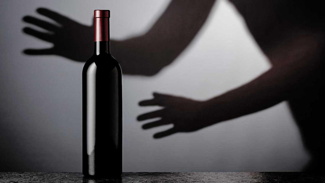 Eine Weinflasche steht im Vordergrund, dahinter ist ein Schatten mit zwei Händen zu sehen, die die Flasche stehlen wollen