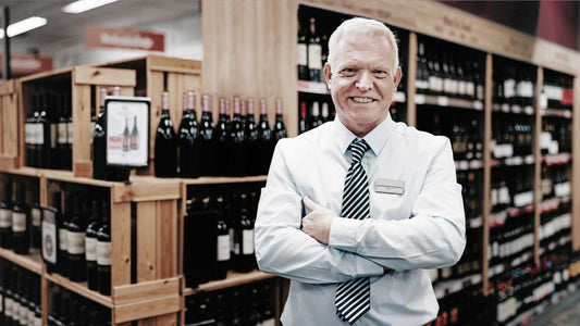 Ein Weinhändler steht in einer Weinhandlung umgeben von Wein in Weinregalen