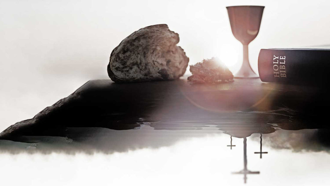 Ein Weinkelch und eine Bibel stehen im Vordergrund, mehre Kreuze spiegeln sich im Wasser bei Sonnenuntergang