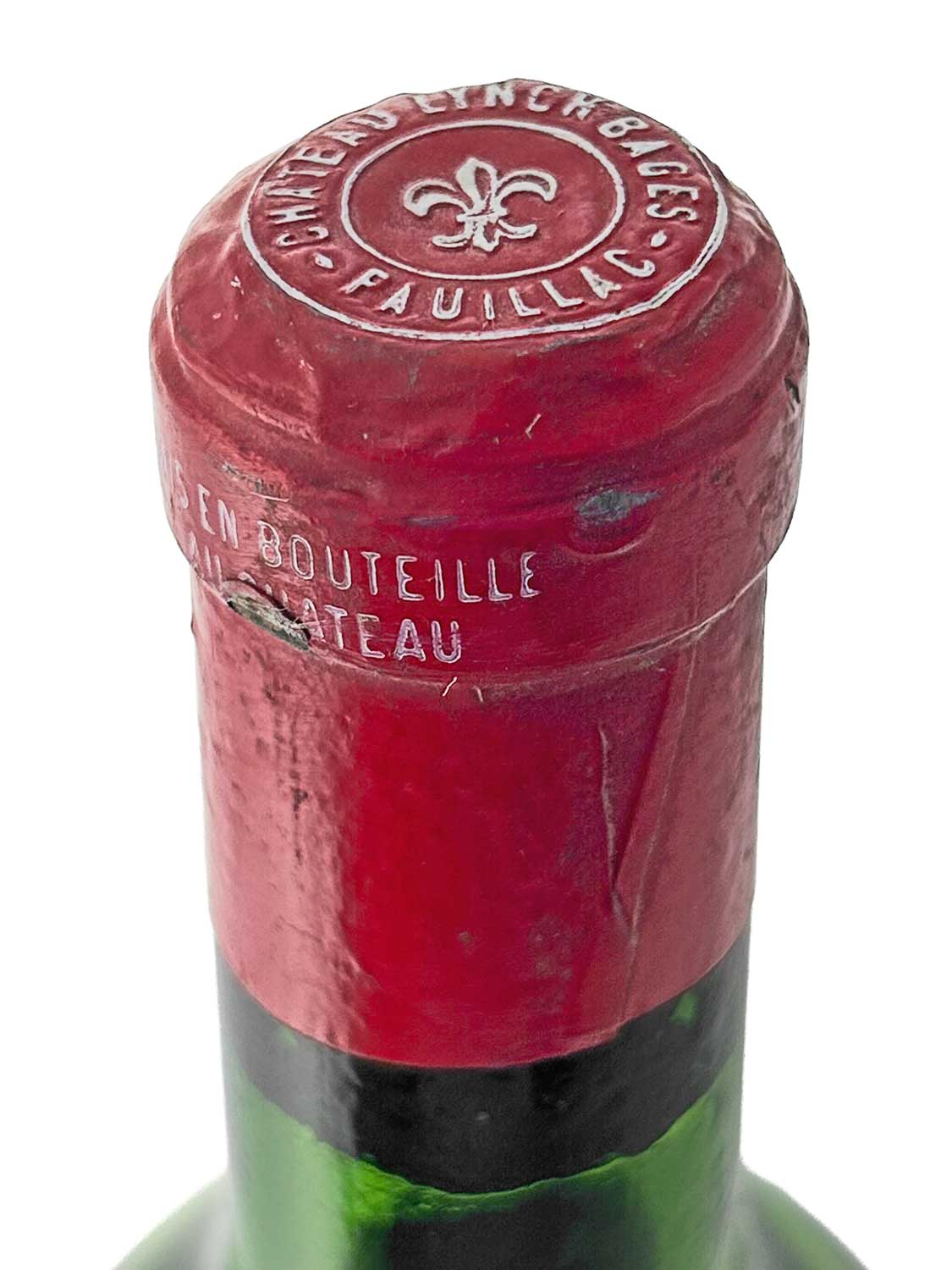 Nahaufnahme des Flaschenhalses einer Weinflasche mit rotem Kapselverschluss, auf dem oben 'CHÂTEAU LYNCH-BAGES PAUILLAC' und ein Lilien-Symbol geprägt sind.
