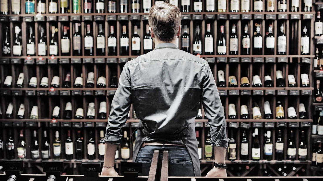 Ein Mann steht vor einem Weinregal in einer Weinhandlung mit viel Flaschen Bordeaux-Wein und verschiedenen Jahrgängen