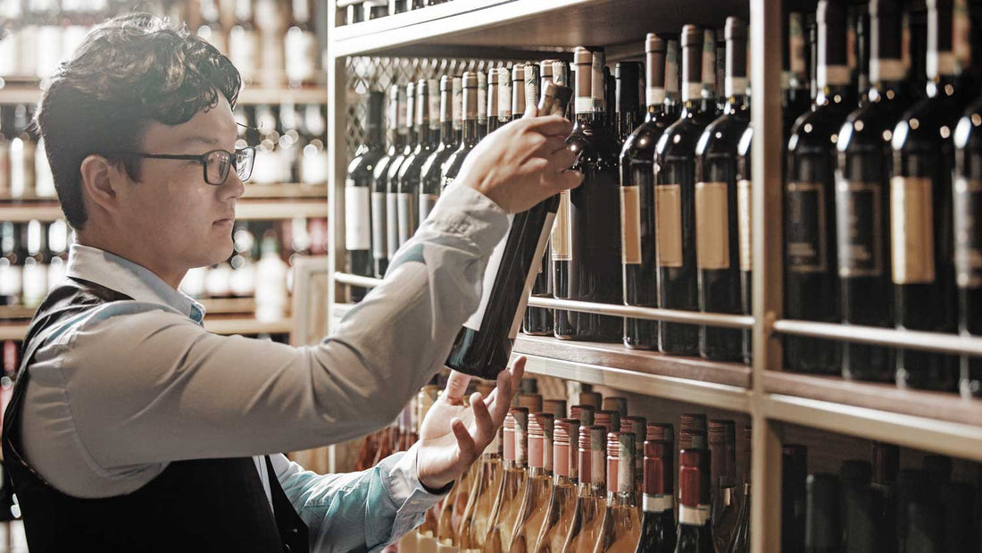 Weinhändler schaut sich eine Weinflasche in einer Weinhandlung an