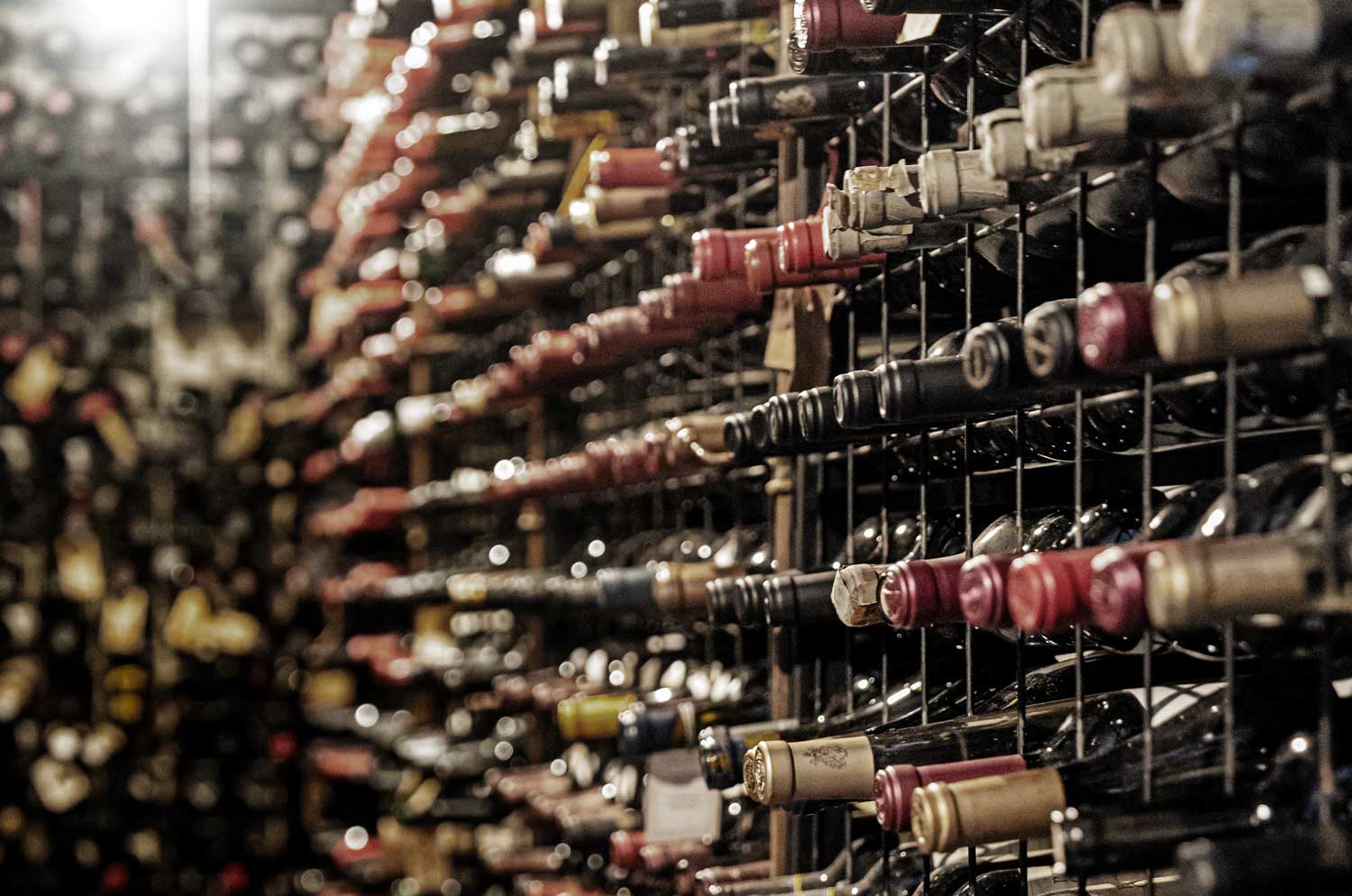 Weinkeller mit Regalen voller Bordeaux-Weinflaschen, die horizontal gelagert sind, mit verschiedenen Kapselfarben und Etiketten.