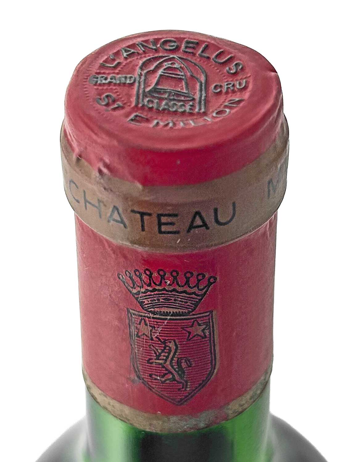 Nahaufnahme des roten Flaschenhalses einer Weinflasche mit dem Aufdruck 'CHATEAU' auf dem goldfarbenen Band und einem Wappen mit Krone sowie dem Schriftzug 'L'ANGELUS GRAND CRU CLASSE' auf dem Kapselverschluss.