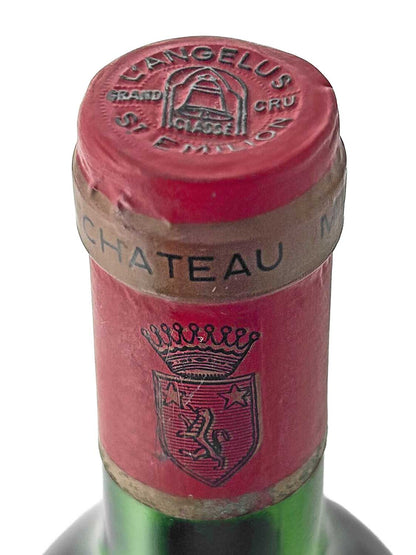 Nahaufnahme des roten Flaschenhalses einer Weinflasche mit dem Aufdruck 'CHATEAU' auf dem goldfarbenen Band und einem Wappen mit Krone sowie dem Schriftzug 'L'ANGELUS GRAND CRU CLASSE' auf dem Kapselverschluss.