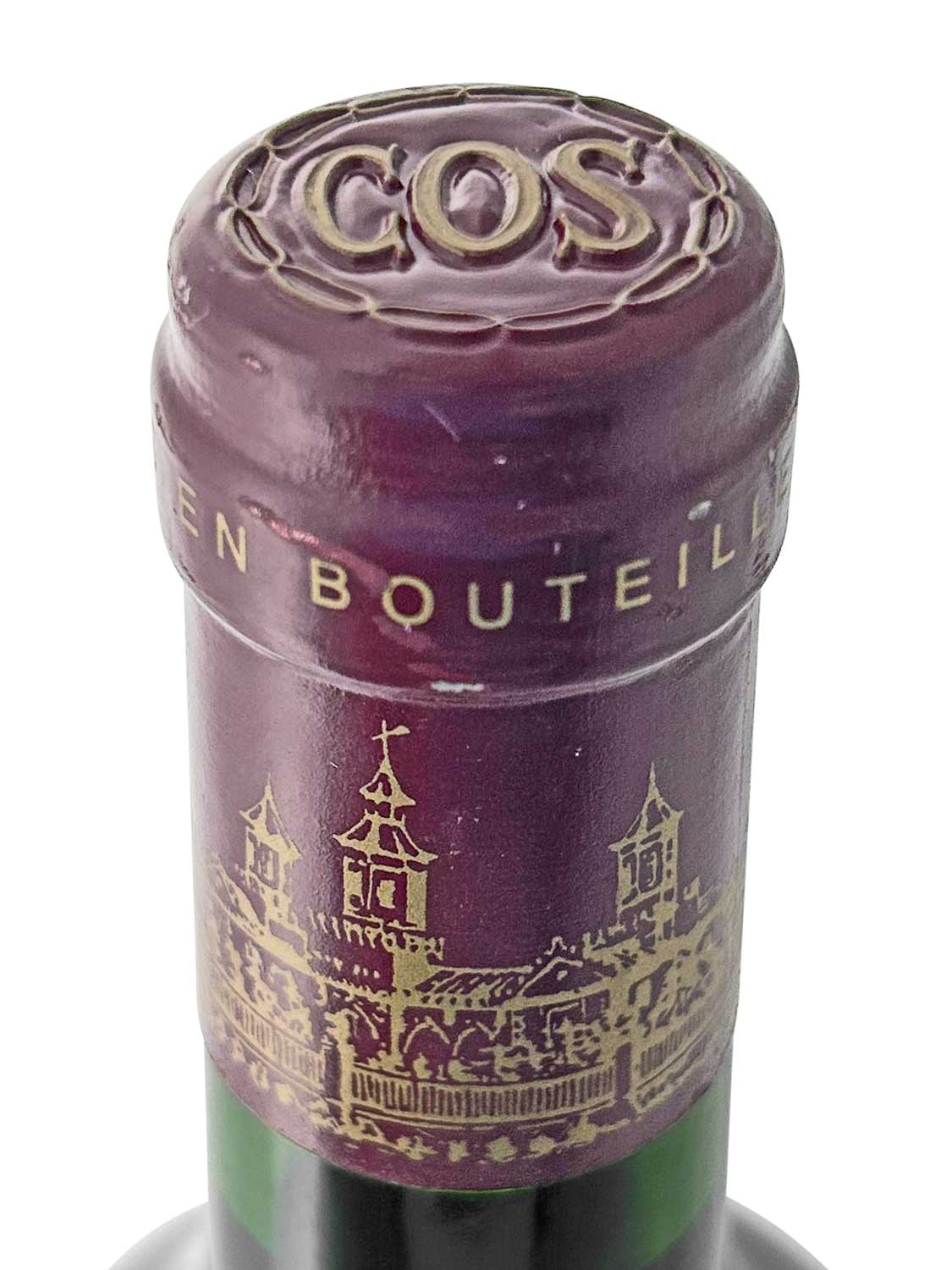 Verschlusskapsel einer Rotweinflasche von Chateau Cos d'Estournel, Jahrgang 1999, mit goldener Prägung 'COS' und Schlosszeichnung auf dunkelrotem Metall.