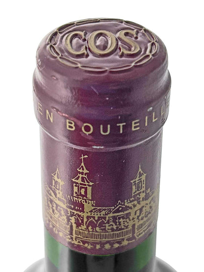 Verschlusskapsel einer Rotweinflasche von Chateau Cos d'Estournel, Jahrgang 1999, mit goldener Prägung 'COS' und Schlosszeichnung auf dunkelrotem Metall.