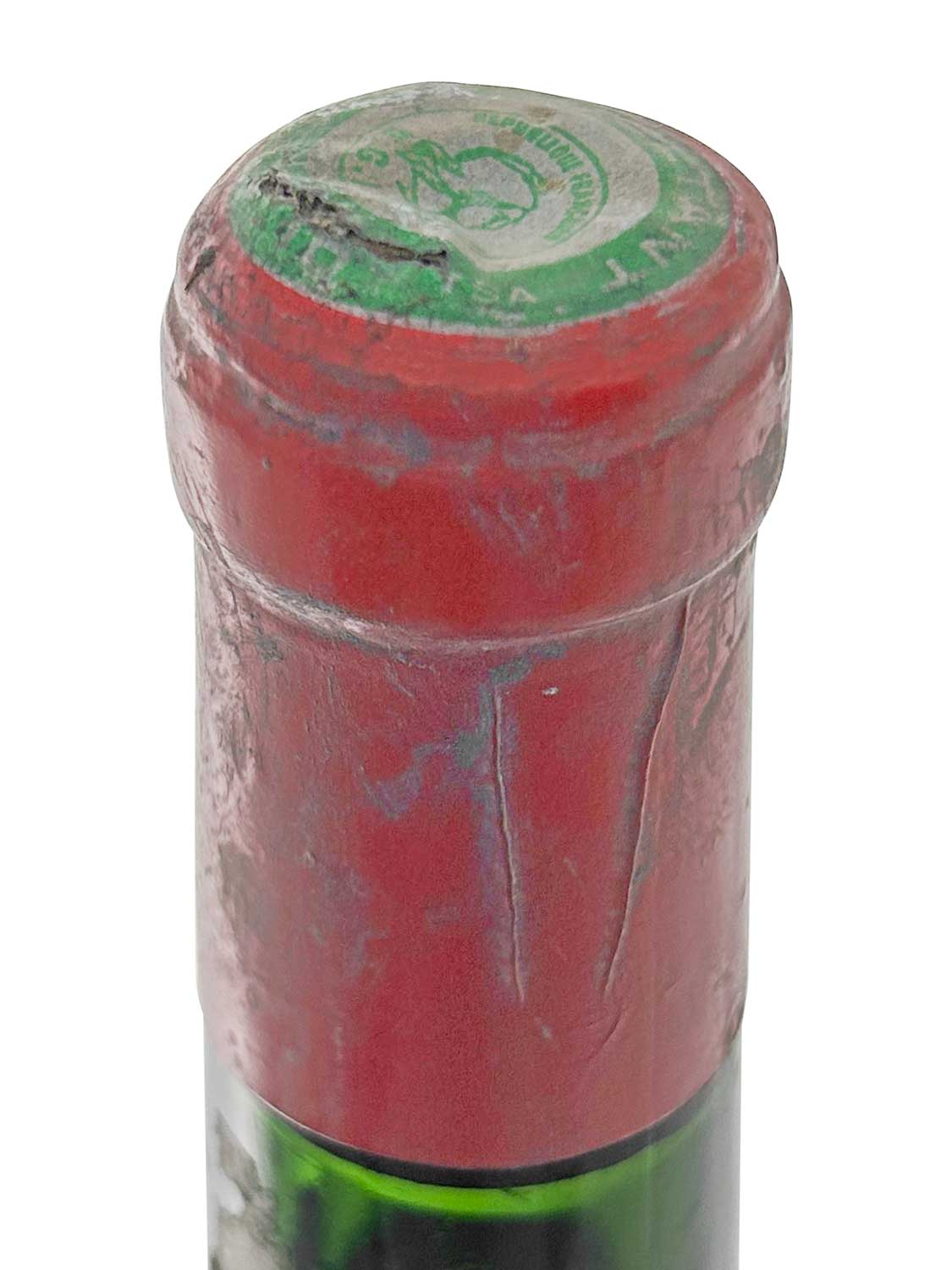 Nahaufnahme des Flaschenhalses einer Weinflasche mit rotem Siegel und grüner Kapsel, teilweise beschädigt.