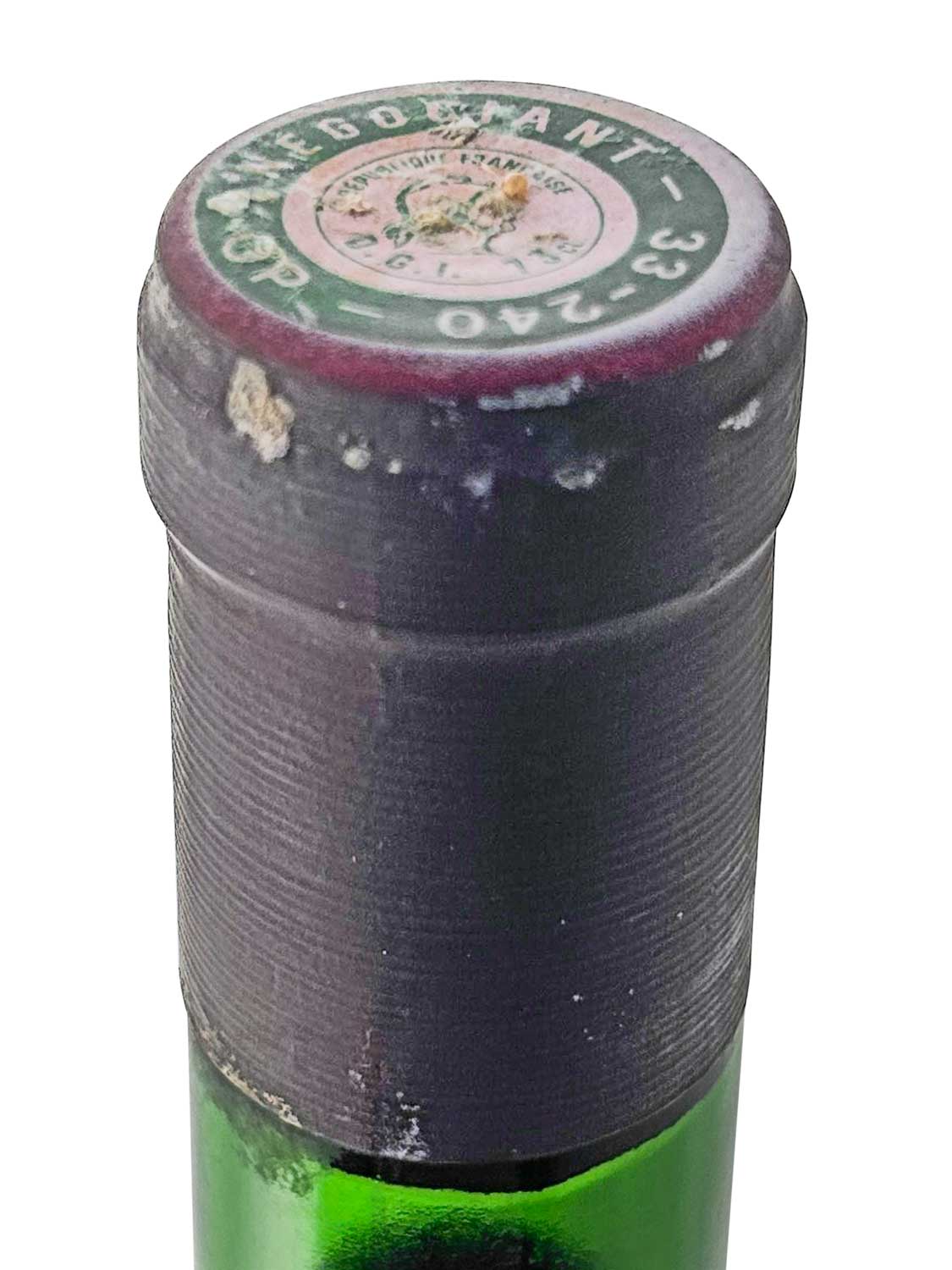 Flaschenkapsel eines grünen Weinflaschenhalses mit abgenutztem, dunkelrotem Siegel und rundem Etikett oben mit teilweise lesbarem Text.