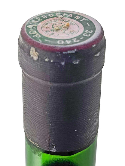 Flaschenkapsel eines grünen Weinflaschenhalses mit abgenutztem, dunkelrotem Siegel und rundem Etikett oben mit teilweise lesbarem Text.