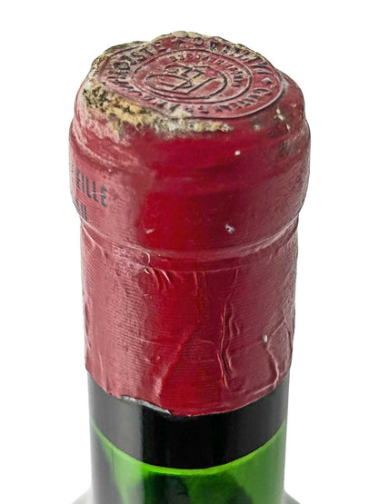 Nahaufnahme des roten Kapselverschlusses einer Weinflasche mit geprägtem Siegel und sichtbaren Gebrauchsspuren.