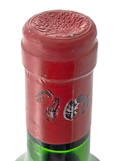 Grüner Weinflaschenhals mit rotem Kapselverschluss, geprägt mit Traubenmotiv, teilweise abgeblätterte schwarze Schriftzeichen auf der Kapsel.