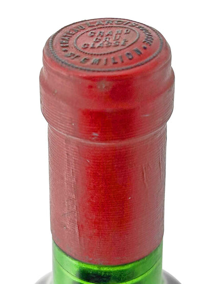 Roter Flaschenverschluss mit geprägtem Text 'CHATEAU LARCIS DUCASSE GRAND CRU CLASSE SAINT-EMILION' auf grünem Flaschenhals.